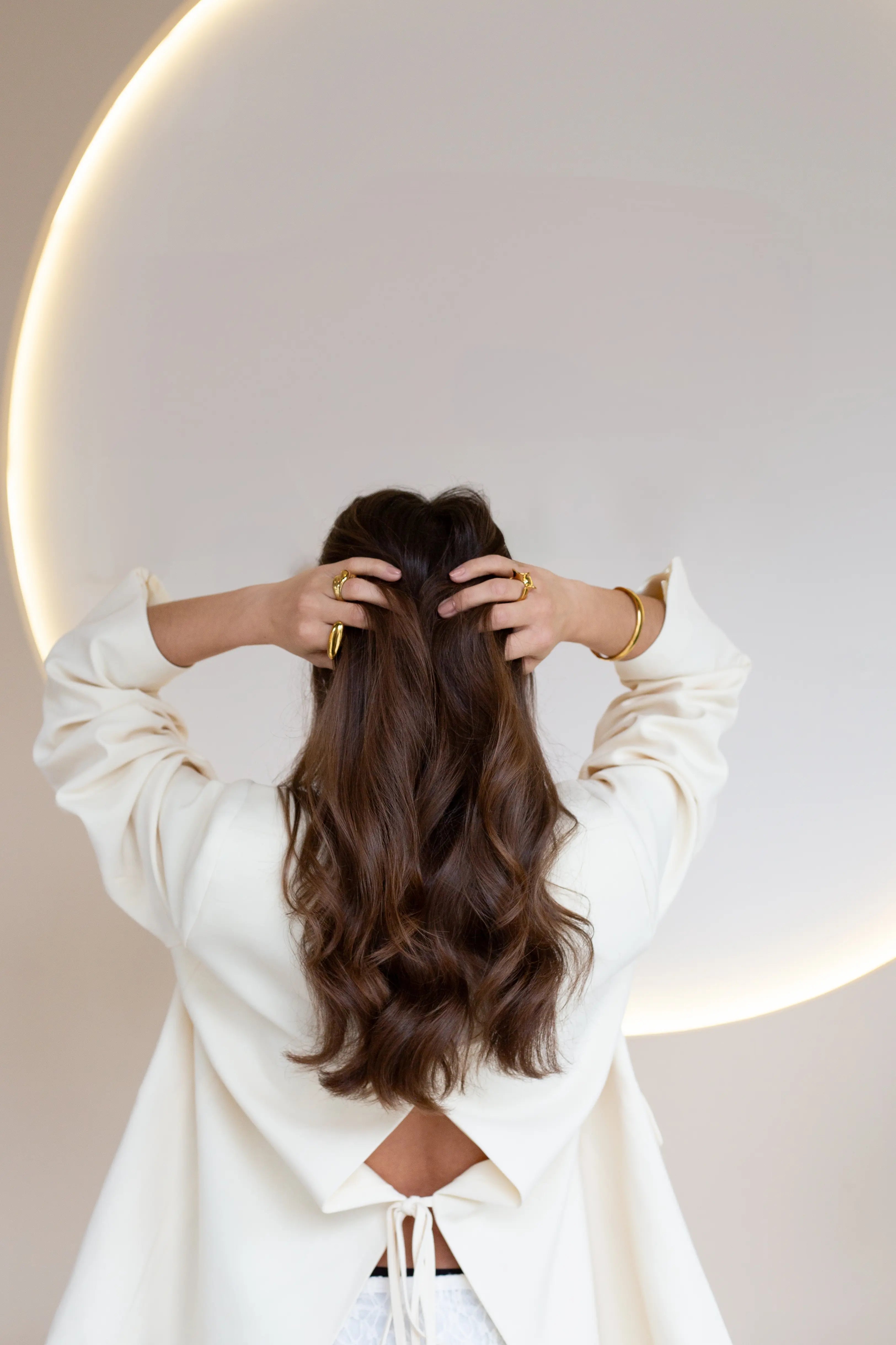 Modelo con joyas doradas en manos y muñecas, peinado suelto y fondo minimalista